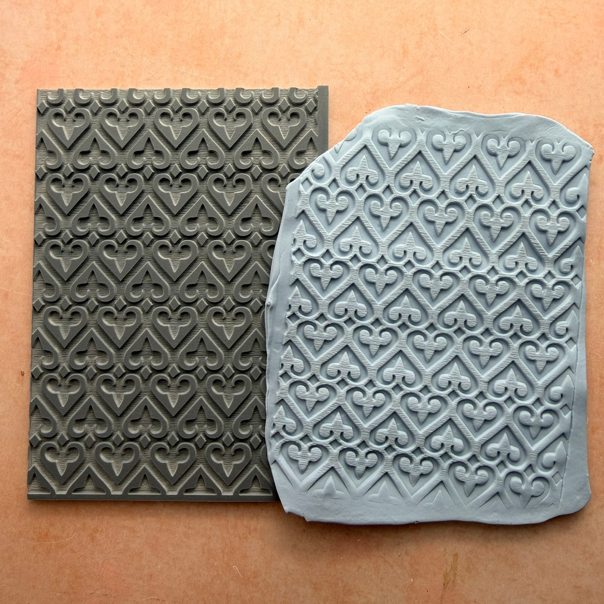 Heart of Fleur 3x4 inch rubber stamp beside impressed polymer clay slab showing repeating heart and fleur-de-lis lattice pattern