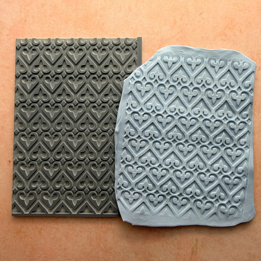 Heart of Fleur 3x4 inch rubber stamp beside impressed polymer clay slab showing repeating heart and fleur-de-lis lattice pattern